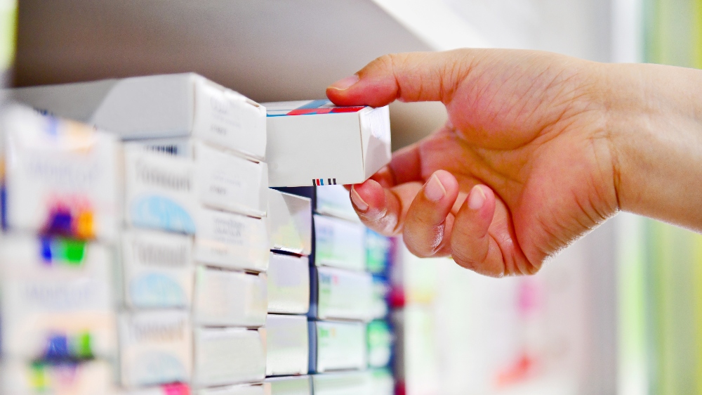 Close up image of pharmacist's hand grabbing a drug box from a shelf